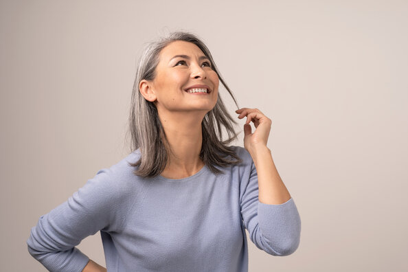 Portrait einer schönen Frau mit grauen Haaren und blau-grauem Pullover, die glücklich mit einer Haarsträhne spielt