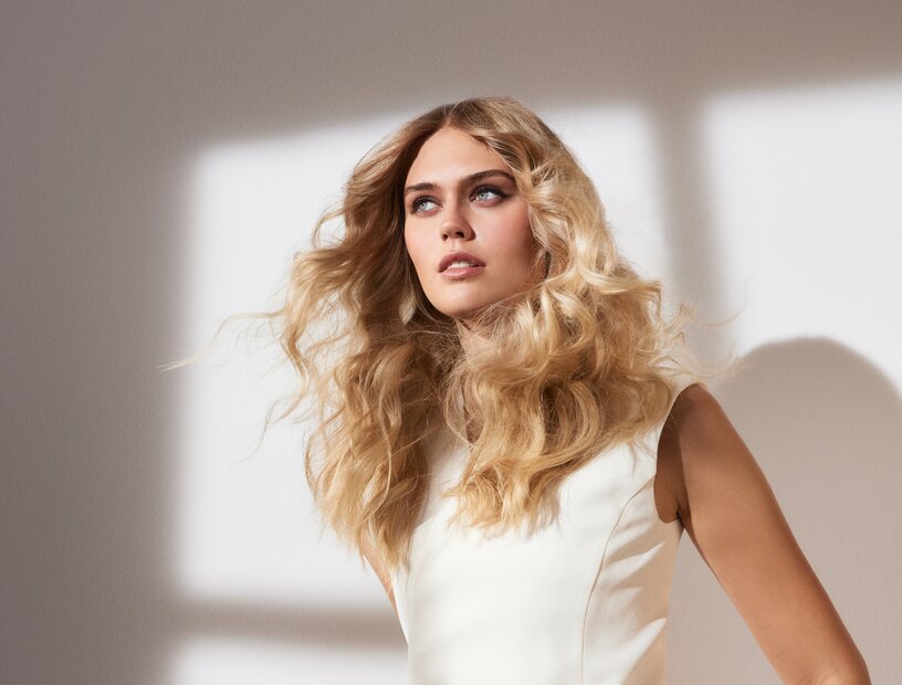 Eine Frau mit schönem, langem, glänzendem, welligem Haar als Sinnbild für die richtige Haarpflege bei trockenen Haaren im Winter